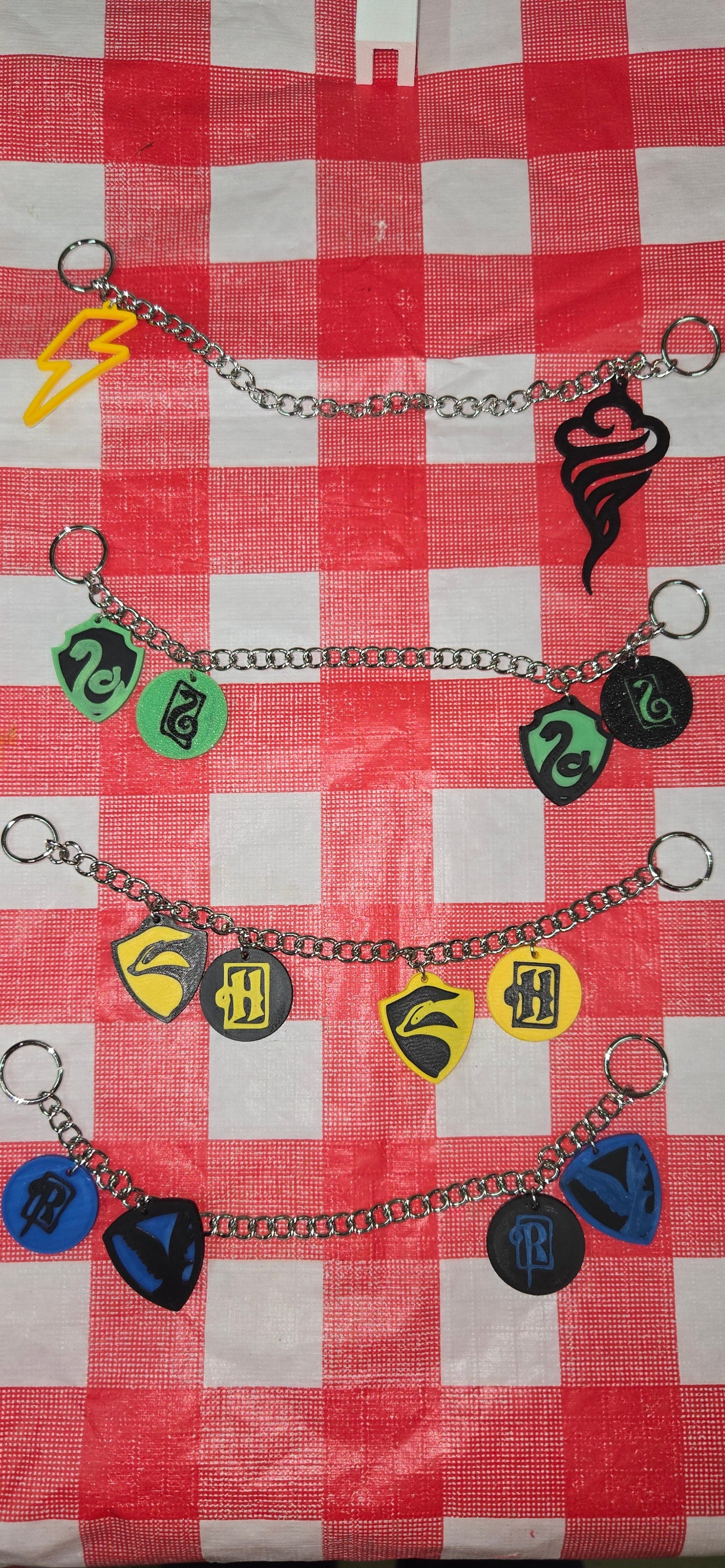 Set of guitar pick holder chains with colorful picks on a red and white checkered tablecloth.